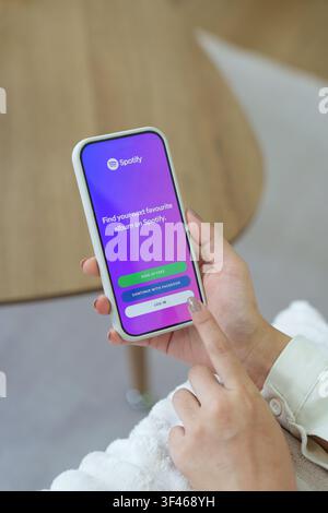 Girl in the room holding a smartphone with Spotify Music app on the screen. Wooden bridge Stock Photo
