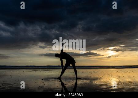 Person doing yoga on a wet beach at sunset Stock Photo