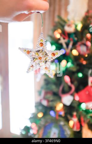 Person hanging a sparkly star ornament on Christmas tree Stock Photo