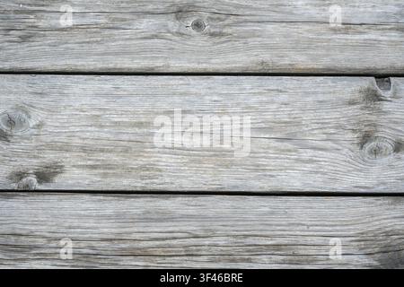 A high-angle, close-up shot of weathered wooden planks arranged horizontally. The wood features a faded silvery-gray color with prominent natural grai Stock Photo