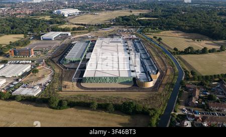 Aerial view of a large modern data center facility with solar panels on the roof, surrounded by green fields, a canal, and suburban housing in Waltham Stock Photo