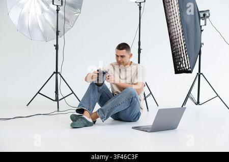 Young man photographer, viewing photos and videos on camera, transfering pictures to laptop for retouch Stock Photo