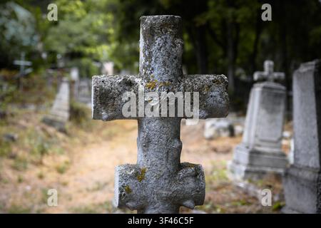 A close-up photograph of an old, weathered stone cross in a cemetery. The cross features a rough, textured surface with patches of yellow lichen and a Stock Photo