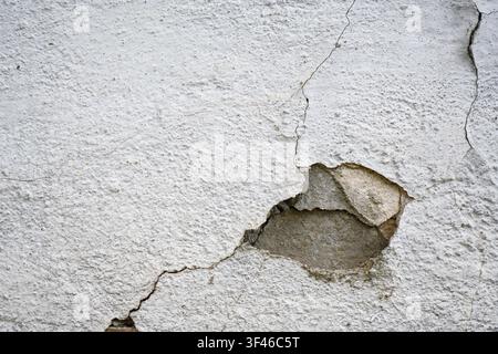A close-up view of a weathered white wall featuring a rough, stucco-like texture. A large section of the outer plaster layer has broken away, revealin Stock Photo