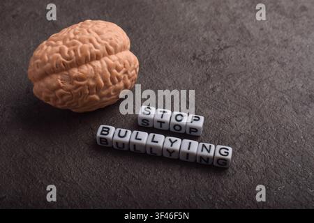 Brain model beside stop bullying text on textured dark background, representing mental health impact, psychological harm, and awareness campaign Stock Photo