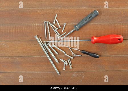 Screwdrivers and metal screws arranged on wooden surface with copy space Stock Photo