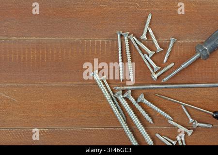 Screwdrivers and metal screws arranged on wooden surface with copy space Stock Photo