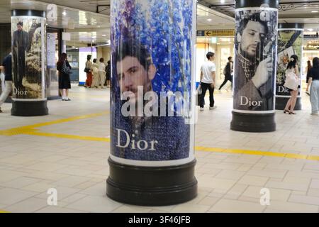 Dior brand advertising campaign wrapped around structural pillars in a busy Japanese train station concourse with commuters in the background. Stock Photo