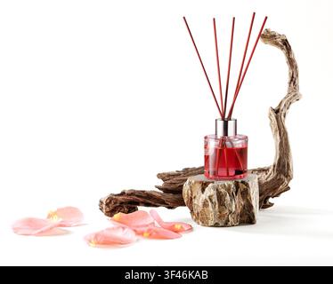 Rose essence reed diffuser bottle on a stone stand beside driftwood and rose petals isolated on white background. Stock Photo