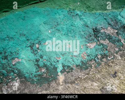 Close-up of a weathered concrete wall with peeling turquoise paint, revealing rough grey plaster texture, cracks, and natural grunge details. Stock Photo