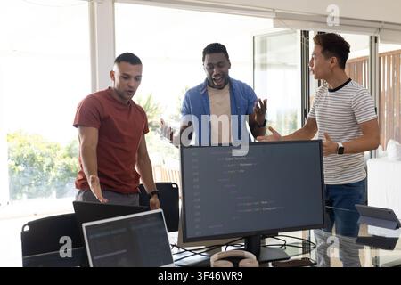Diverse male coworkers discussing code on large monitor at modern office with laptops Stock Photo