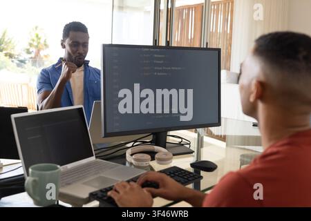 African American male coworkers coding at glass desk with code on monitor, copy space Stock Photo