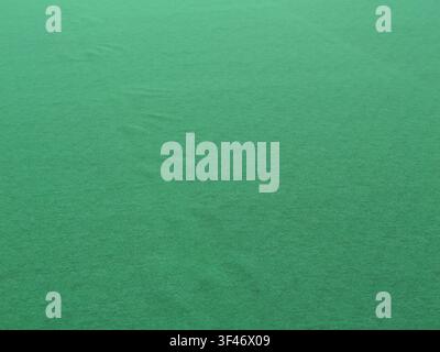 Close-up of a smooth green felt fabric texture with a soft matte finish and subtle folds, creating an abstract and minimal background. Stock Photo
