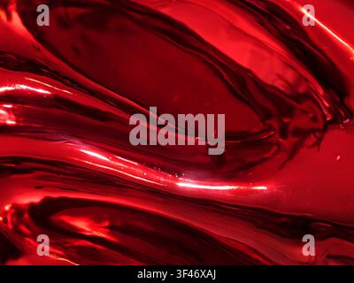 Close-up of a glossy, reflective red metallic surface with smooth fluid waves, bright highlights, and deep shadows creating an abstract, dynamic textu Stock Photo