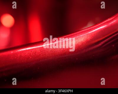 Close-up of a smooth, glossy metallic red surface with a sharp bright highlight line and a soft bokeh background creating an abstract, modern aestheti Stock Photo