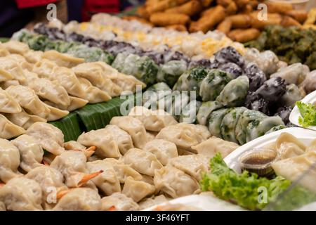 A close-up view of assorted handmade dumplings, spring rolls, and traditional Asian snacks neatly displayed on banana leaves at a local food market. Stock Photo