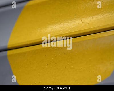 Close-up of a textured yellow painted metal surface with small surface bubbles and a distinct panel gap against a grey background. Stock Photo