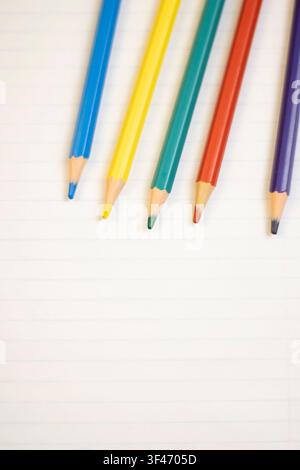 Colorful Pencils Arranged on Lined Paper for School or Creative Writing Theme; Vertical Stock Photo