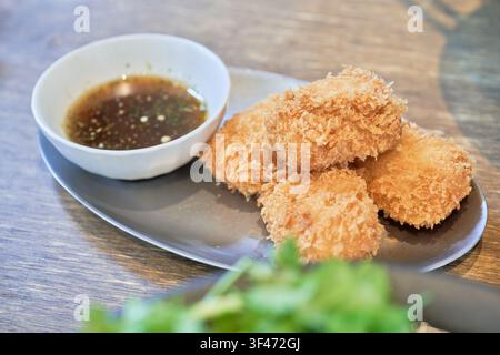 Golden brown crab croquettes and dark dipping sauce on a sleek grey plate over a rustic wooden table highlighting delicious Asian gourmet appetizers. Stock Photo