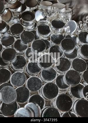Overhead view shows many round brushed silver metal cups packed together in repeating rows, with reflective highlights, worn texture, and curved edges Stock Photo