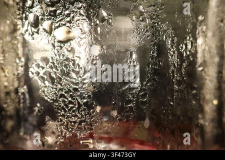 A condensation on glass with scattered water droplets catching warm light, abstract textured surface conveying cozy atmosphere and close up detail Stock Photo