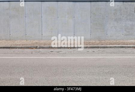 Prefab concrete wall at roadside with tiled sidewalk and street in front. Background for copy space. Stock Photo
