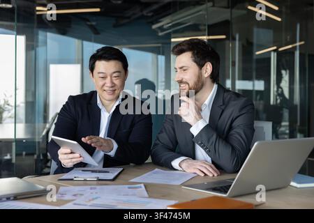 Two diverse business partners discussing digital strategy and financial data during a meeting in a modern office, fostering collaboration and professional teamwork Stock Photo