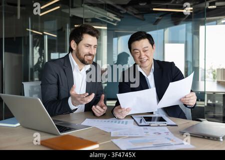 Diverse business executives smiling and analyzing reports. Actively brainstorming ideas and celebrating achievements in a modern office environment Stock Photo