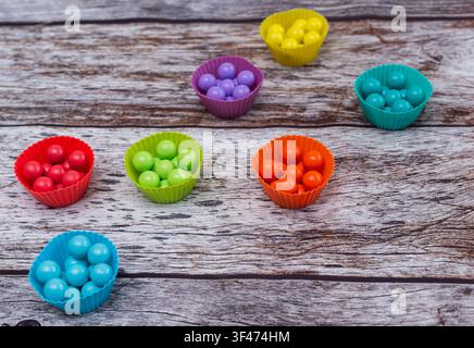 Colorful balls sorted into silicone cups lie on rustic wooden background. Bright plastic spheres promote early child development through color matchin Stock Photo