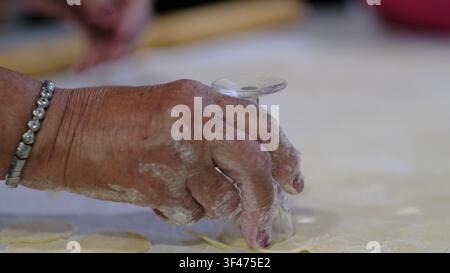 Person uses the rim of a glass to cut circular shapes from thin pastry dough on a kitchen work surface. The clip illustrates food preparation at home Stock Photo