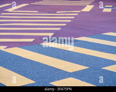 Close-up of a paved urban road intersection with yellow pedestrian crosswalk stripes, grey asphalt, and a reddish-purple surface texture. Stock Photo