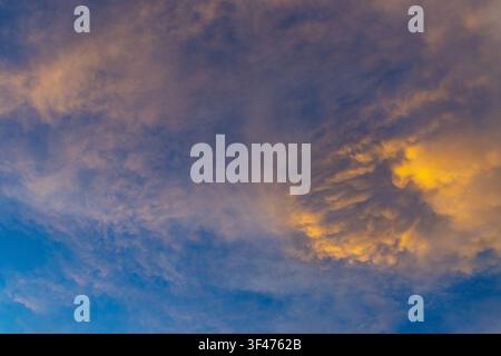 A golden cloud at sunset with blue sky, dramatic textured cloud formation, warm light illuminating cloud edges, atmospheric mood and soft gradient sky Stock Photo