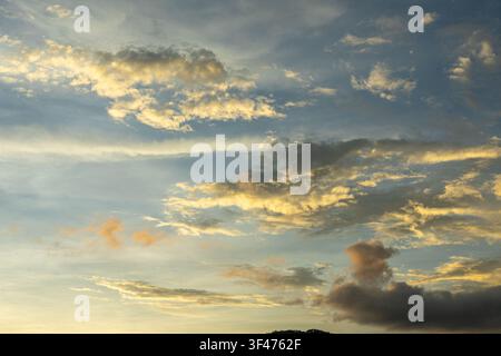 A golden cloud at sunset sky, soft blue sky, layered cloud formation, warm light, serene atmosphere, horizon silhouette Stock Photo