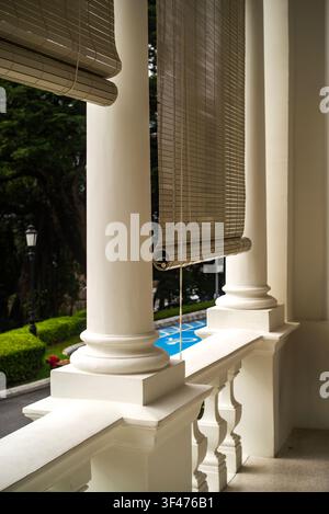 Bamboo chick blinds hanging on a white colonial building veranda overlooking lush greenery in a heritage property. Stock Photo