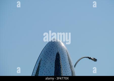 Sleek minimalist composition of a polished perforated metallic sculpture against a clear blue sky. Reflective surfaces and industrial textures evoke t Stock Photo