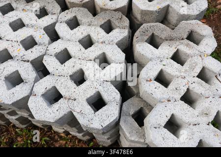 A stacked concrete paving blocks with hexagonal outer shape and square center holes arranged in neat pattern on ground, textured gray surface with sca Stock Photo