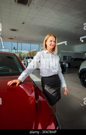 Female salesperson smiling, standing next to new red car Stock Photo