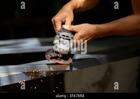 A worker hands using angle grinder on metal frame producing sparks in workshop, close up view of tool and steel surface with dynamic motion and warm l Stock Photo