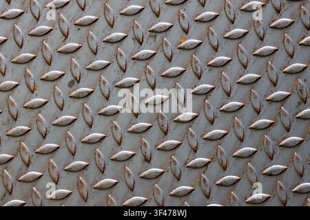 A worn metal diamond plate with rust spots and raised teardrop tread pattern, industrial texture conveying age and grit Stock Photo