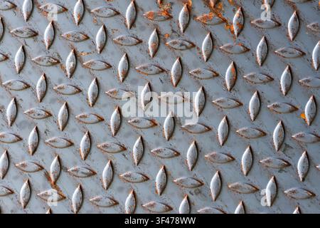 A worn metal diamond plate texture with rust spots and raised pattern, industrial background with gray paint flaking and orange corrosion throughout s Stock Photo