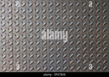 A worn metal diamond plate texture with rust spots and repeating raised tread pattern, industrial floor surface conveying rugged utilitarian character Stock Photo
