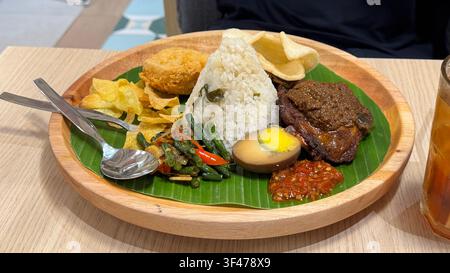 Traditional Indonesian meal featuring white rice, beef, vegetables, boiled egg and sambal served on a banana leaf-lined plate. Stock Photo