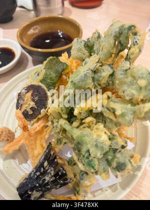Assorted Japanese tempura featuring crispy battered vegetables and seafood served with dipping sauce at a restaurant. Stock Photo