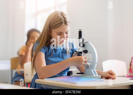 Focused schoolgirl adjusts a microscope during a science lesson Stock Photo