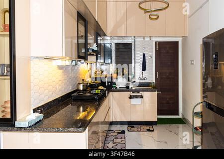 A sleek modern kitchen with glossy beige cabinets, black granite counters, hexagonal back splash, and warm lighting for a stylish, organized look. Stock Photo