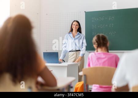 Teacher standing by chalkboard with math equations, engaging with students in classroom Stock Photo