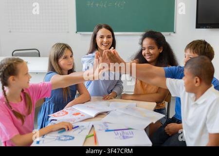 Teacher and diverse schoolchildren join hands in group high five in classroom Stock Photo