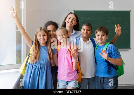 Female teacher and diverse schoolchildren smiling and waving toward the camera Stock Photo