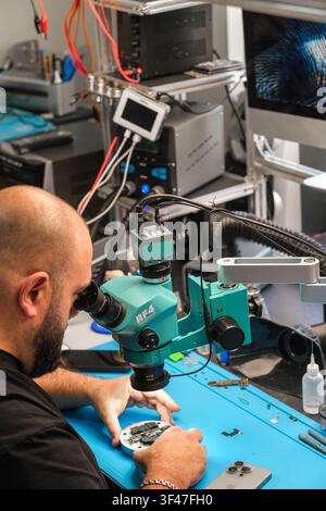Moscow, Russia - July 02, 2026: Technician using microscope to repair electronic device on blue workbench in modern workshop with equipment visible Stock Photo