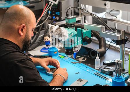 Moscow, Russia - July 02, 2026: Technician repairing smartphone components under microscope in workshop with tools and equipment on blue workbench Stock Photo